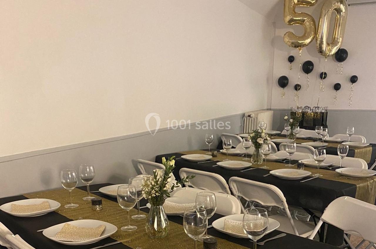 Salle décorée pour un 50e anniversaire avec tables dressées, nappes dorées et ballons dorés et noirs.