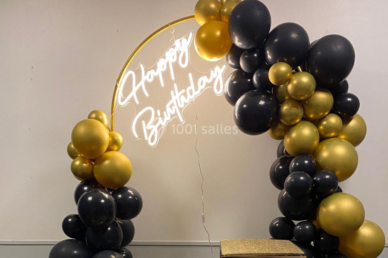 Arc de ballons noirs et dorés avec un néon ’Happy Birthday’ suspendu, décoré pour une célébration festive.