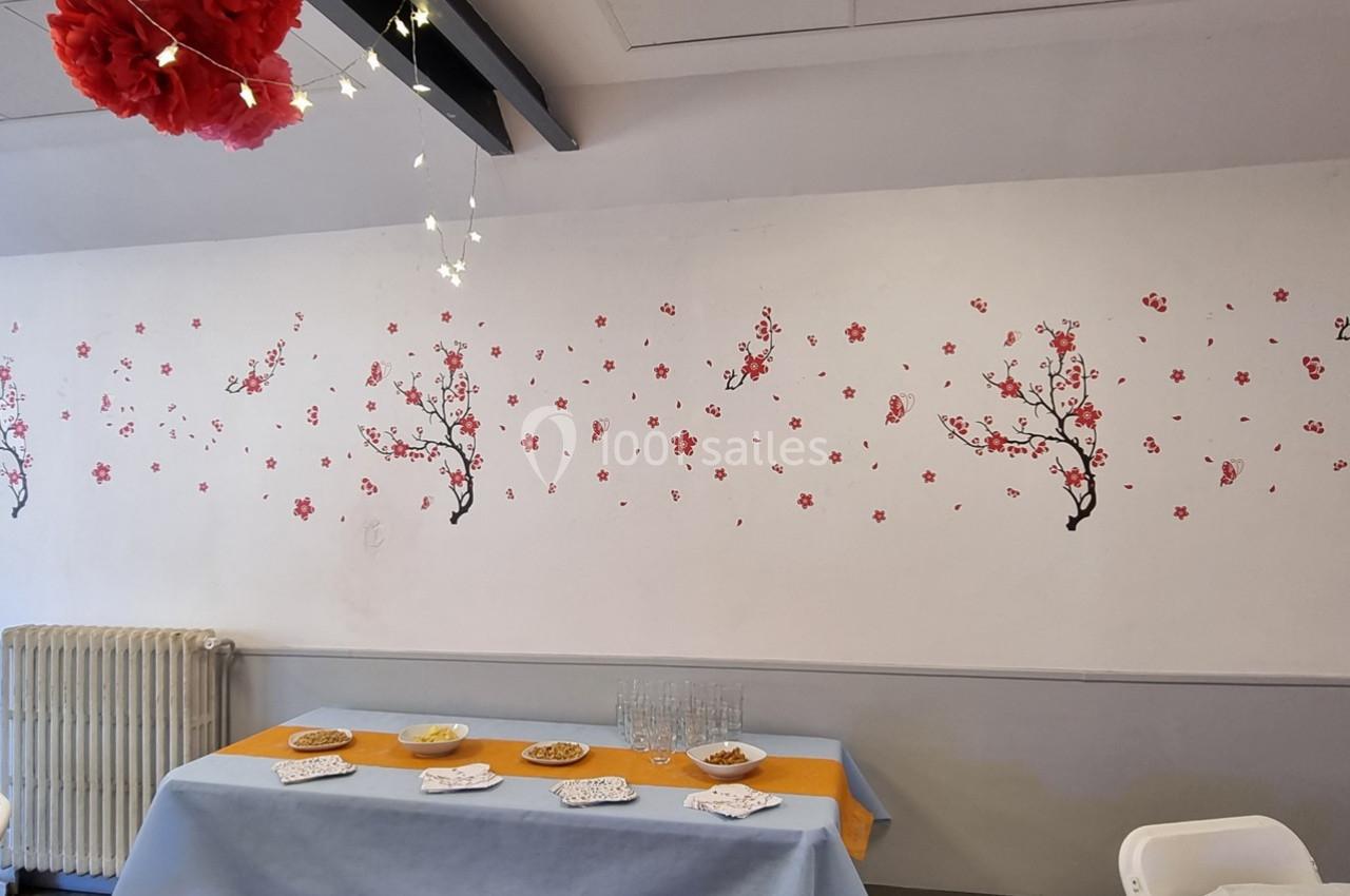Mur décoré de motifs de branches fleuries, table dressée avec nappes colorées et petits plats dans une salle lumineuse.