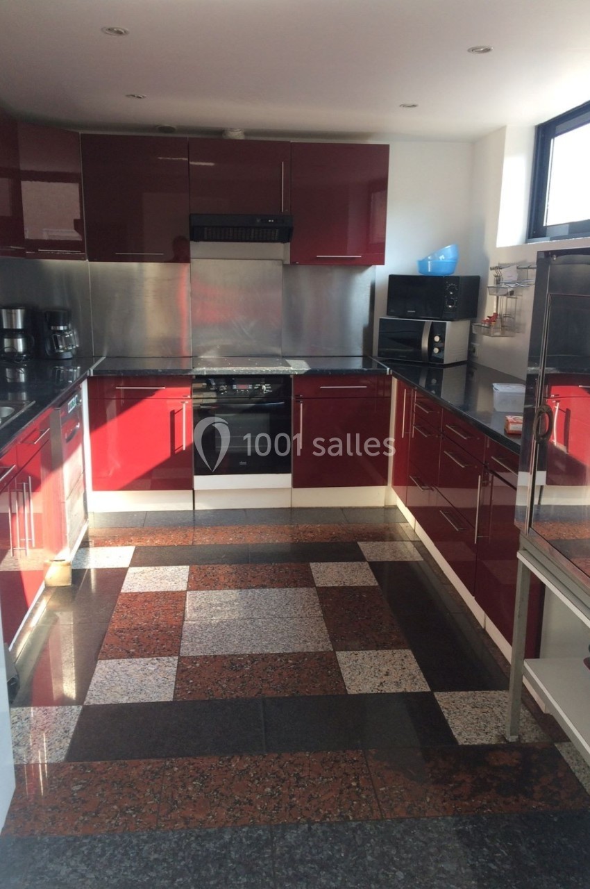 Cuisine moderne avec meubles rouges brillants, plan de travail noir, électroménagers intégrés et sol en carrelage à motifs.