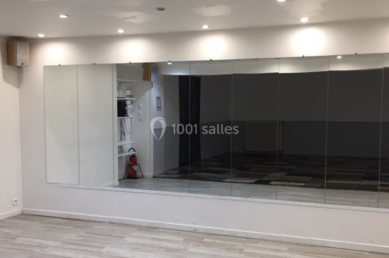 Salle lumineuse avec grand miroir mural, sol en parquet clair et étagères blanches sur le côté.