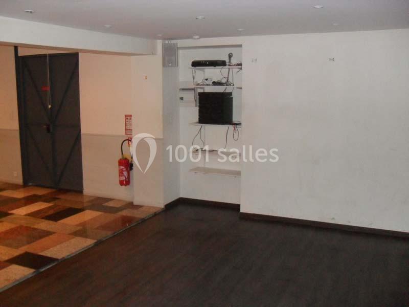 Salle vide avec sol en parquet et carrelage, murs blancs, étagères murales et porte métallique grise.