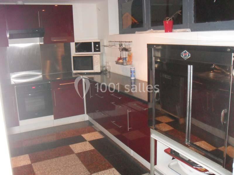 Cuisine moderne avec meubles rouges, plan de travail noir, électroménagers intégrés et carrelage à motifs au sol.