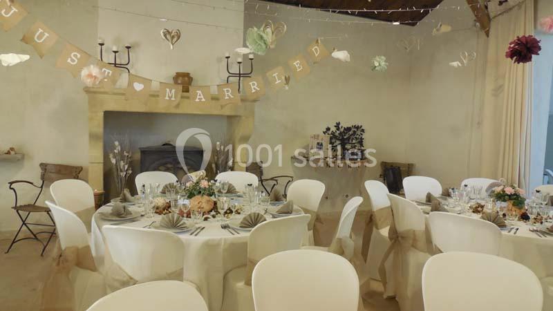 Salle décorée pour une réception de mariage avec tables dressées, guirlande ’Just Married’ et ornements suspendus.