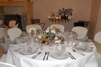 Façade d'une maison provençale avec terrasse ombragée, tables en fer forgé et grand arbre au premier plan.