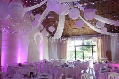 Façade d'une maison provençale avec terrasse ombragée, tables en fer forgé et grand arbre au premier plan.