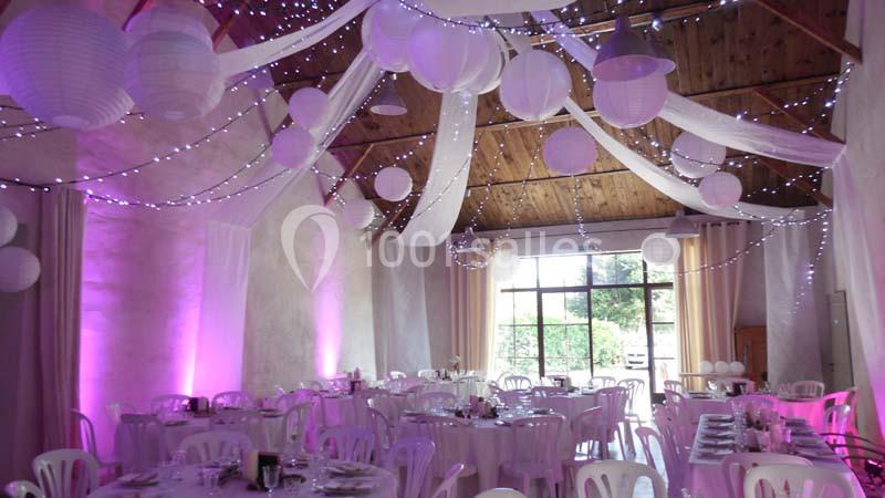 Salle de réception décorée avec des guirlandes lumineuses, des lanternes suspendues et des nappes blanches sur les tables.