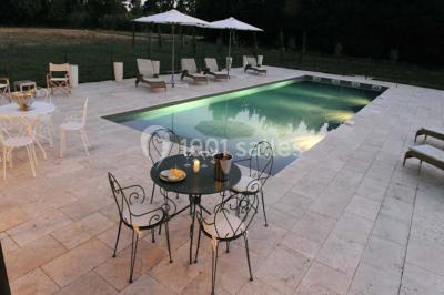 Façade d'une maison provençale avec terrasse ombragée, tables en fer forgé et grand arbre au premier plan.