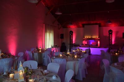 Façade d'une maison provençale avec terrasse ombragée, tables en fer forgé et grand arbre au premier plan.