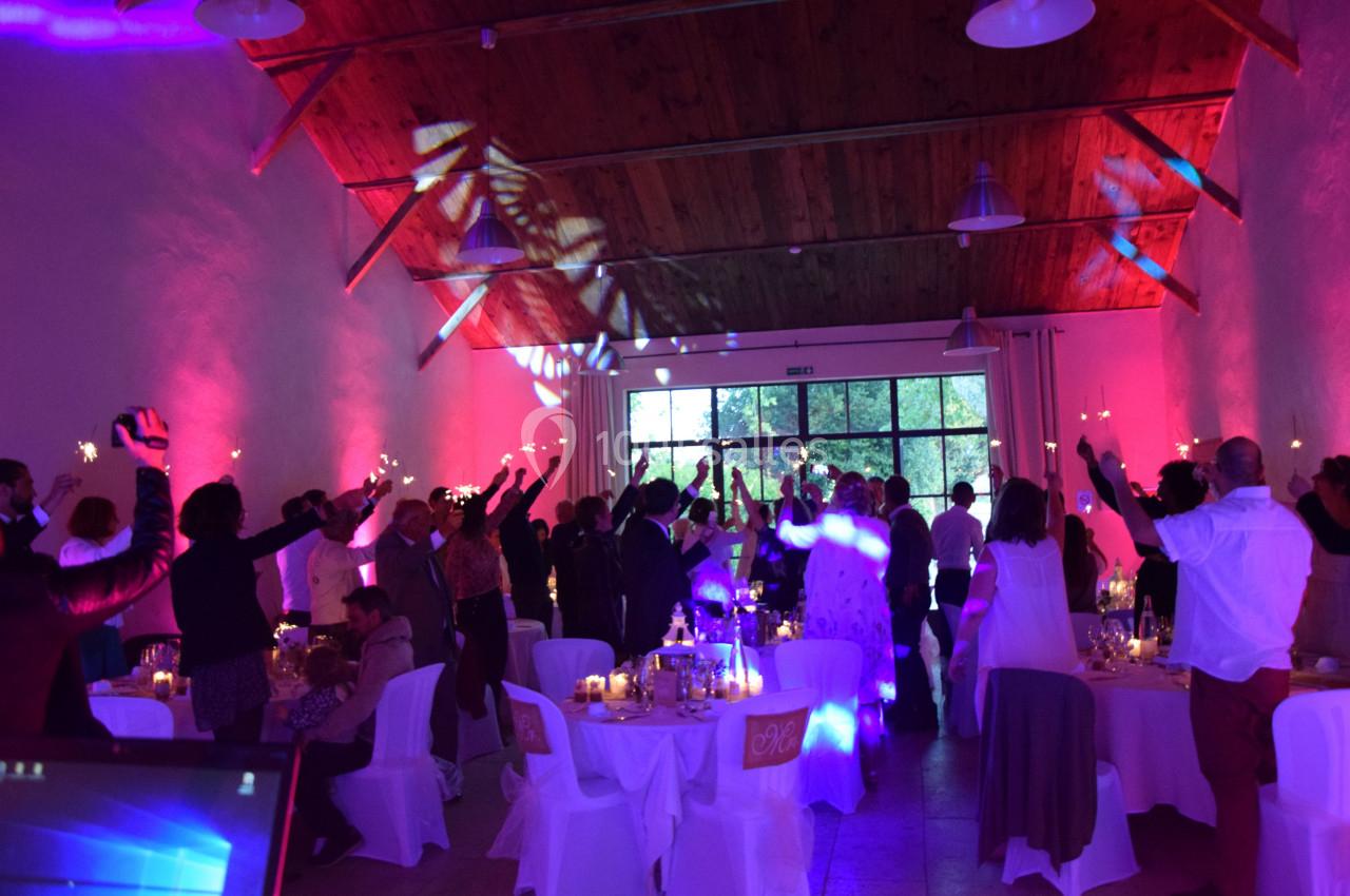 Salle de réception avec invités dansant sous des lumières colorées, tables décorées et ambiance festive.