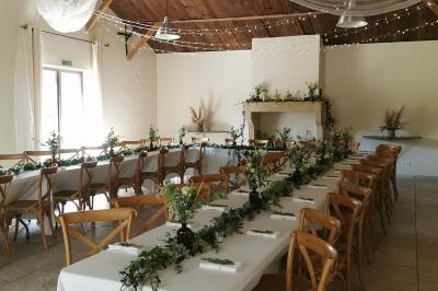 Façade d'une maison provençale avec terrasse ombragée, tables en fer forgé et grand arbre au premier plan.