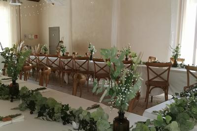 Façade d'une maison provençale avec terrasse ombragée, tables en fer forgé et grand arbre au premier plan.