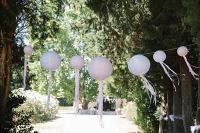 Façade d'une maison provençale avec terrasse ombragée, tables en fer forgé et grand arbre au premier plan.