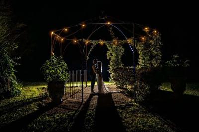 Façade d'une maison provençale avec terrasse ombragée, tables en fer forgé et grand arbre au premier plan.