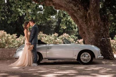 Façade d'une maison provençale avec terrasse ombragée, tables en fer forgé et grand arbre au premier plan.
