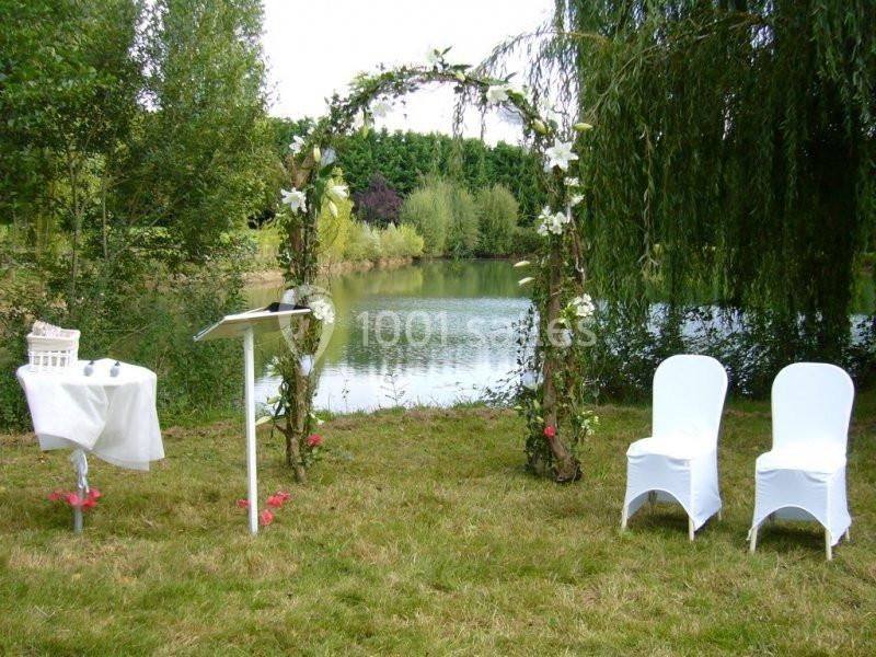 Arche fleurie et chaises blanches installées près d'un lac pour une cérémonie en plein air.