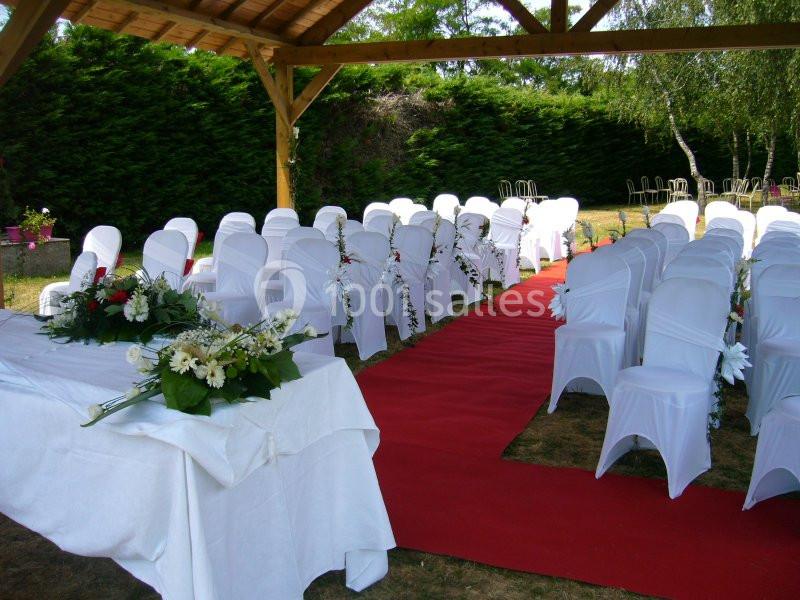 Chaises blanches alignées sous un auvent en bois, avec une allée rouge et des décorations florales.