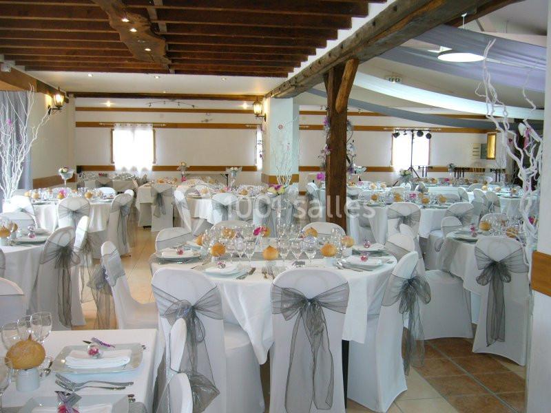 Salle de réception décorée avec des tables rondes, nappes blanches, chaises ornées de nœuds gris et lumière naturelle.