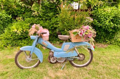 Voiture ancienne bleue décorée de rubans blancs et de fleurs pour une cérémonie, stationnée en extérieur.
