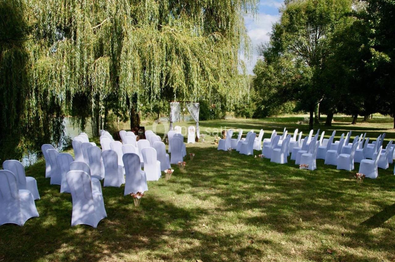 Chaises blanches disposées en extérieur sous des arbres, formant une allée centrale pour une cérémonie en plein air.