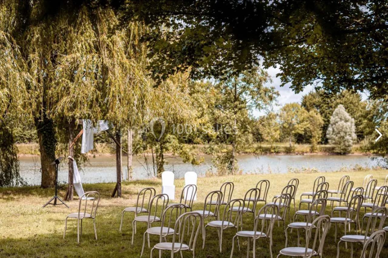 Chaises blanches disposées en extérieur sous des arbres, face à une rivière, pour un événement en plein air.