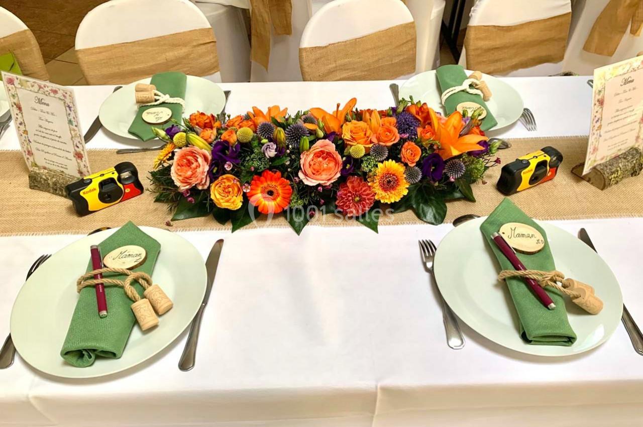 Table décorée avec un chemin en toile de jute, un centre de table floral coloré et des assiettes avec serviettes vertes.