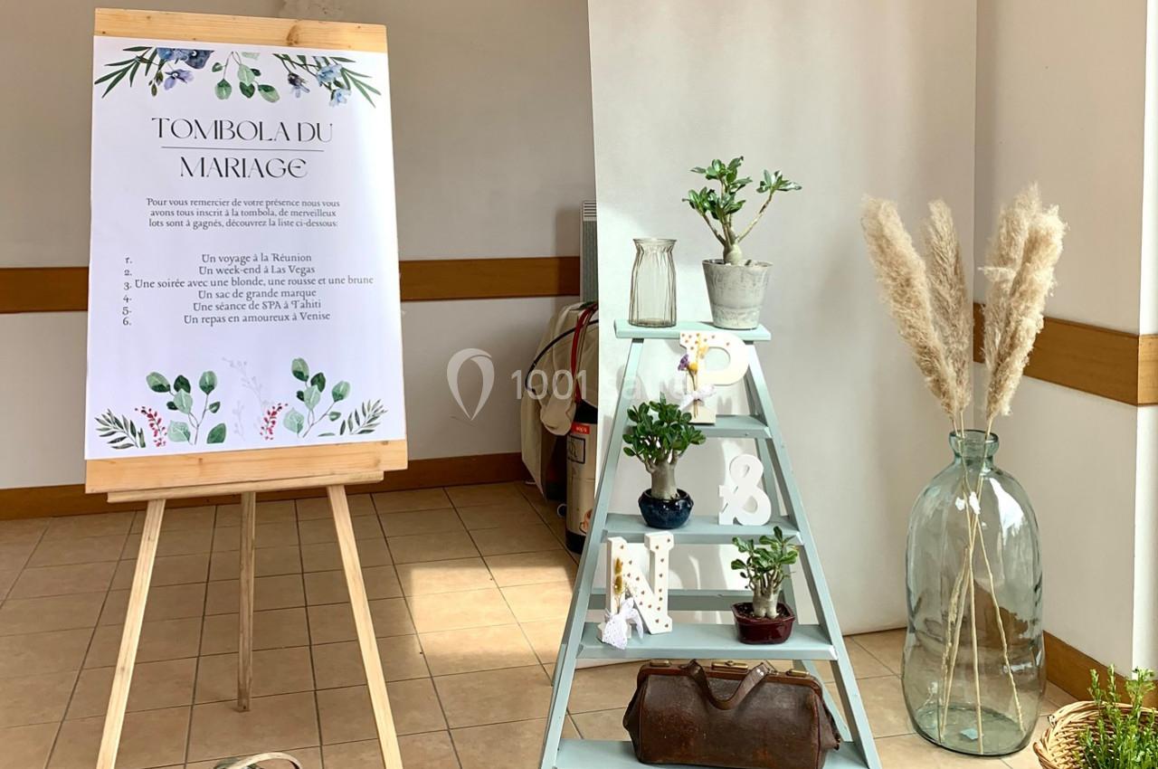 Affiche de tombola de mariage sur un chevalet, décorée de plantes, échelle blanche et accessoires rustiques.