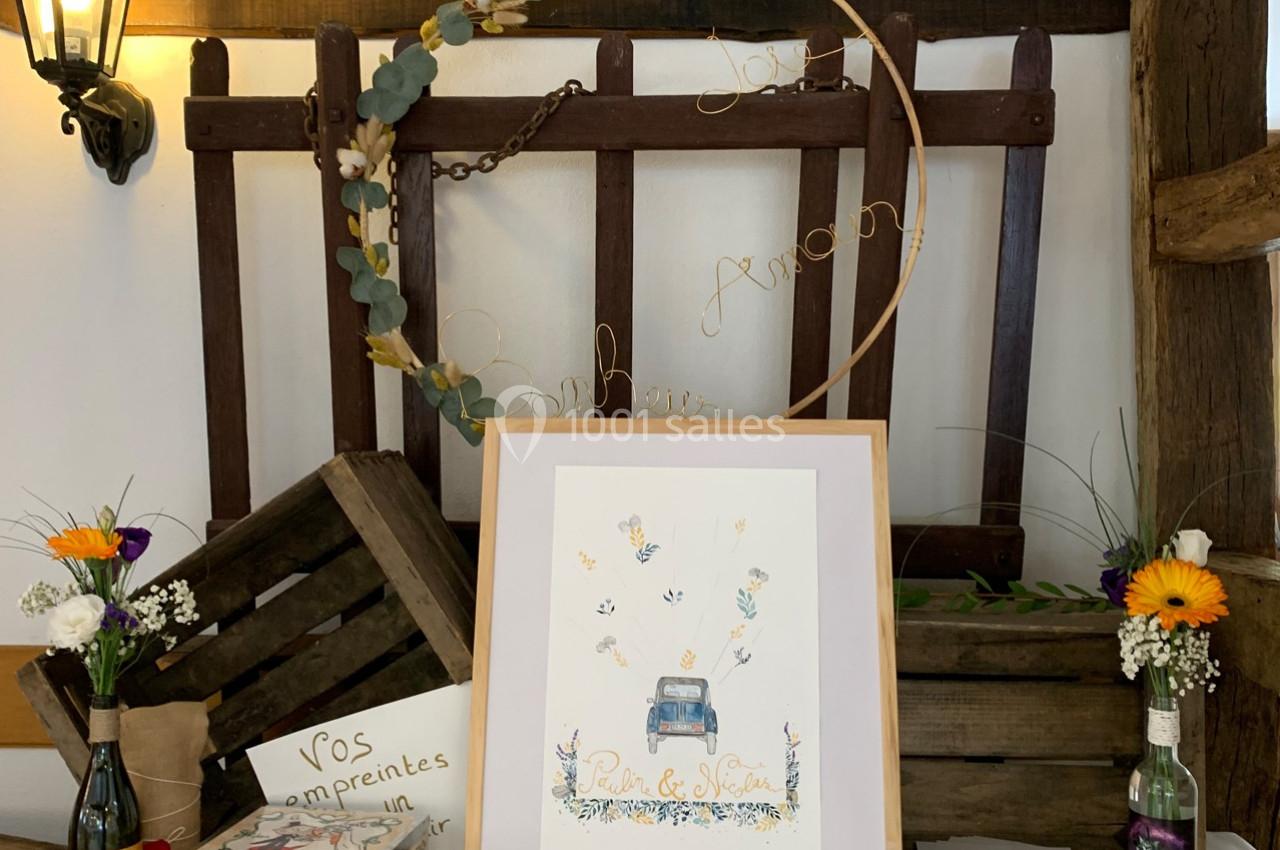 Illustration d'une voiture entourée de papillons, encadrée et posée sur une table décorée de fleurs et d'éléments rustiques.