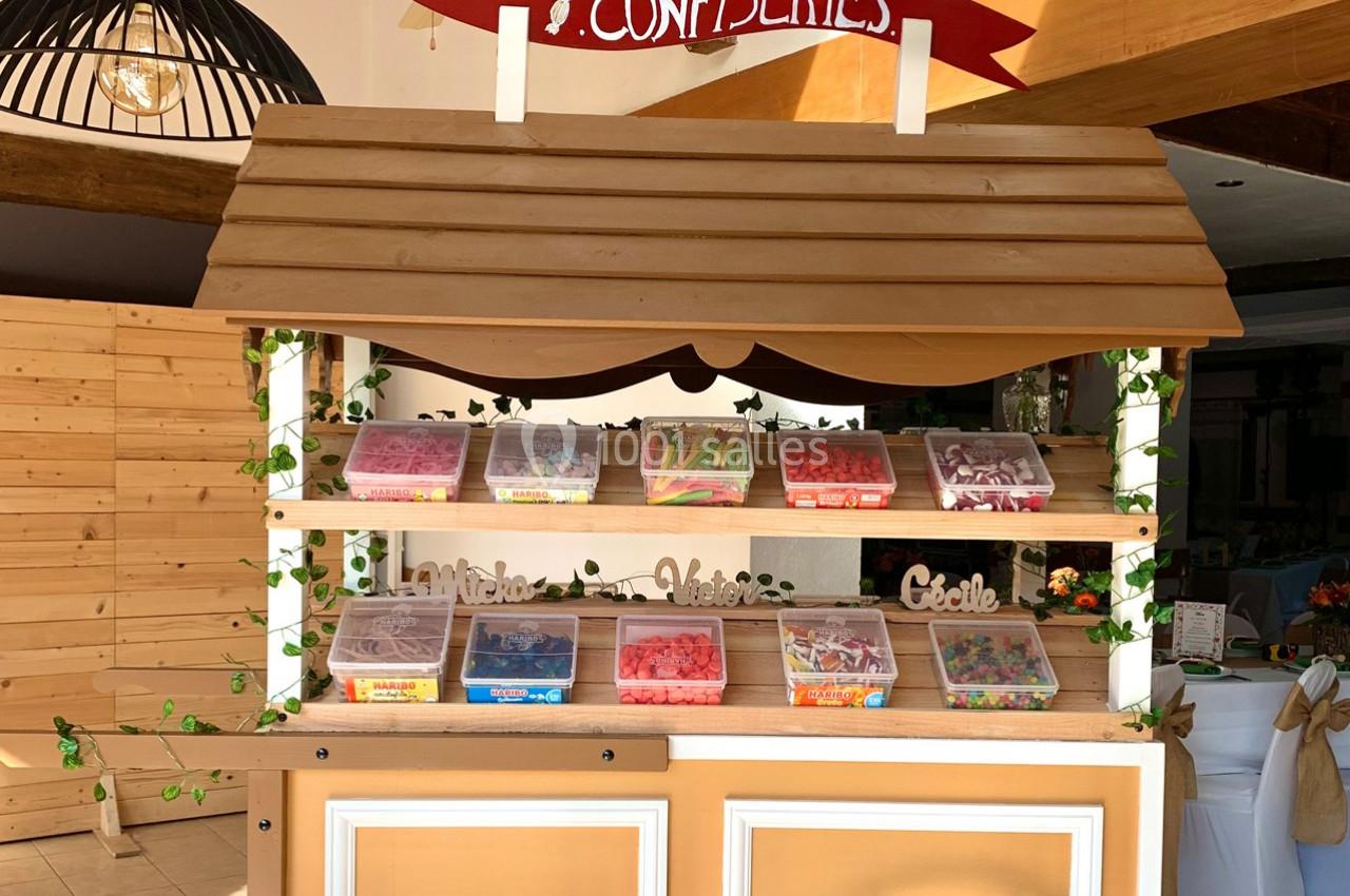 Stand en bois décoré avec des bacs transparents remplis de bonbons colorés, sous une enseigne ’Confiseries’.