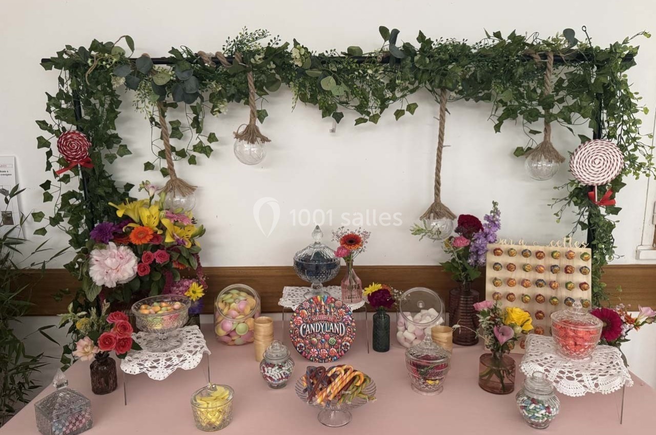 Table décorée avec des fleurs, des bonbons variés et des éléments végétaux suspendus dans un cadre festif.