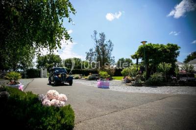 Voiture ancienne bleue décorée de rubans blancs et de fleurs pour une cérémonie, stationnée en extérieur.