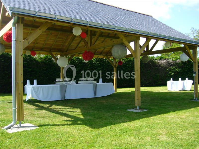 Abri en bois avec toit en ardoise, décoré de lanternes et tables dressées pour un événement en extérieur.