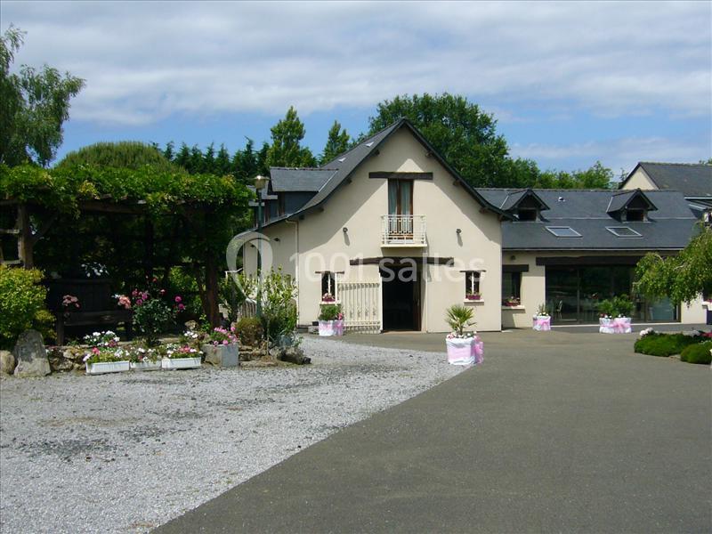 Grande maison beige à deux étages avec jardin fleuri, pergola et allée pavée, entourée de verdure.