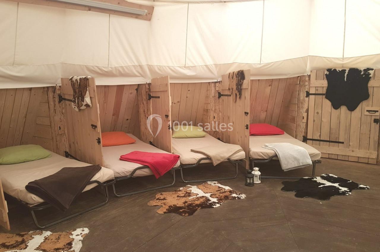 Quatre lits simples avec couvertures colorées dans une pièce circulaire en bois, décorée de tapis en peau.