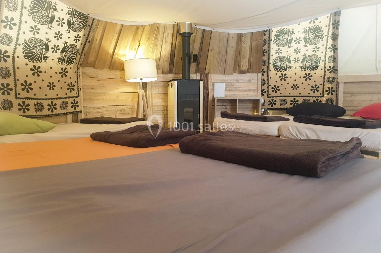 Intérieur d'une tente aménagée avec lits, couvertures, poêle à bois et décoration en bois et tissu.