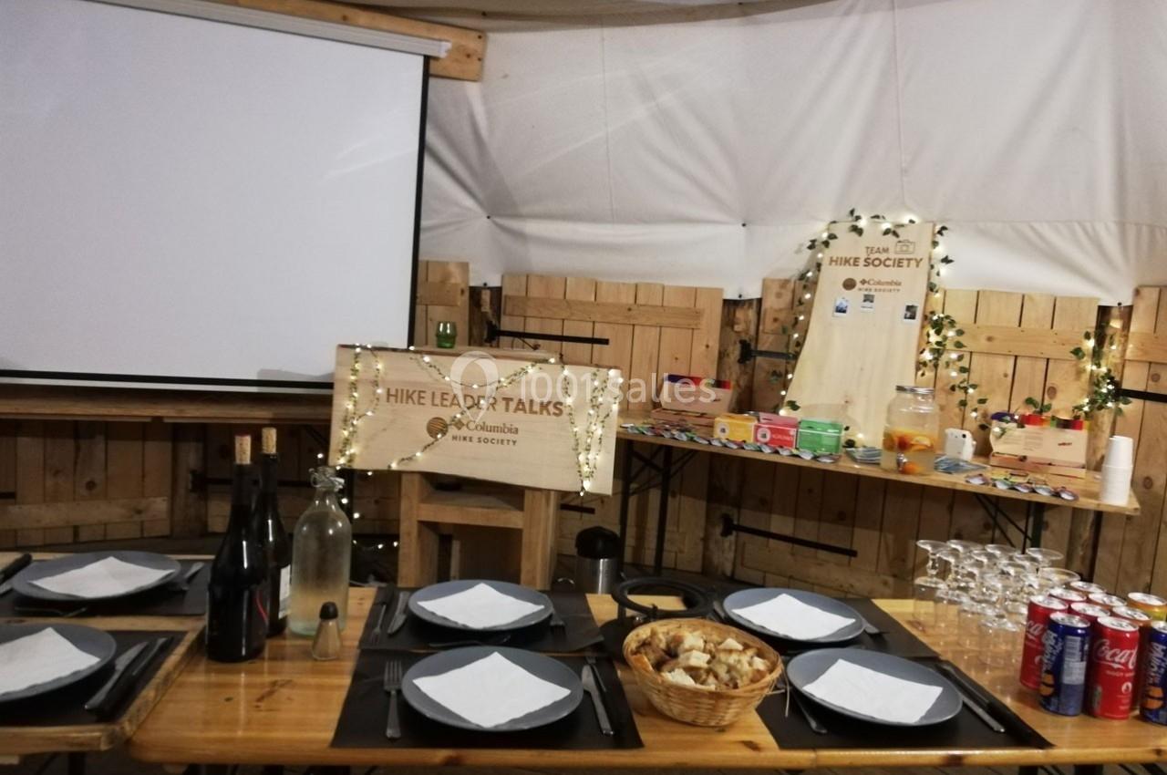 Table dressée avec assiettes et verres devant un écran de projection, décorée pour une présentation ou un événement.