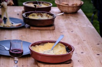 Plat de fromage fondu servi dans des ramequins en terre cuite sur une table en bois, avec du vin rouge et du pain.