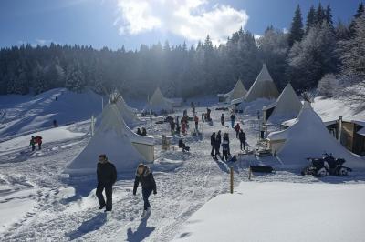 Groupe de personnes rassemblées en extérieur près de tentes et d'une table avec des verres, dans un cadre naturel.
