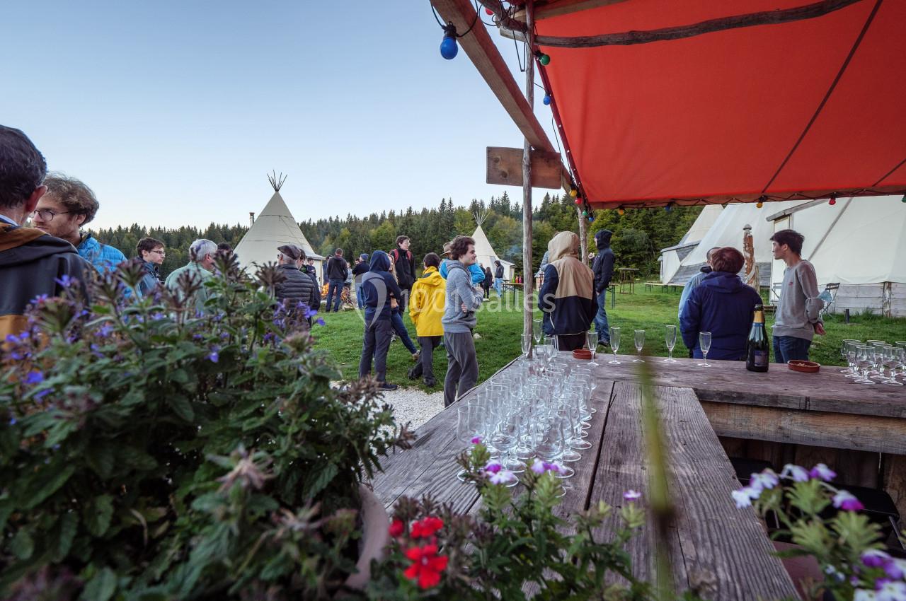 Groupe de personnes rassemblées en extérieur près de tipis, avec une table garnie de verres au premier plan.