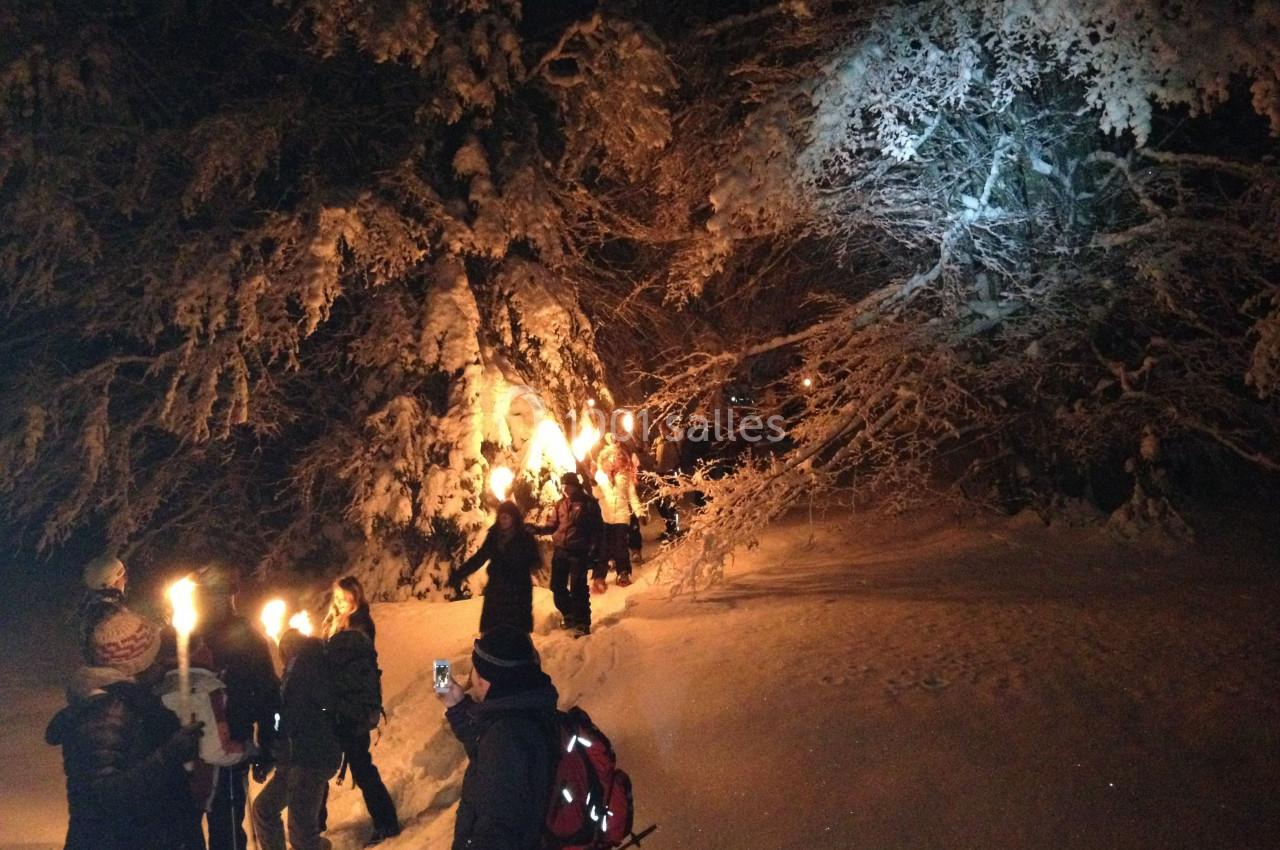 Groupe de personnes marchant de nuit dans une forêt enneigée, éclairées par des torches.