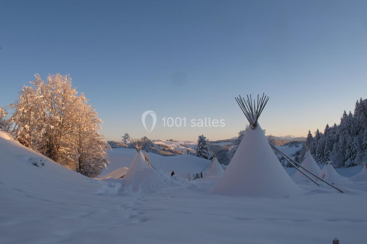 Paysage enneigé au coucher du soleil avec des tipis entourés d'arbres givrés et de collines.