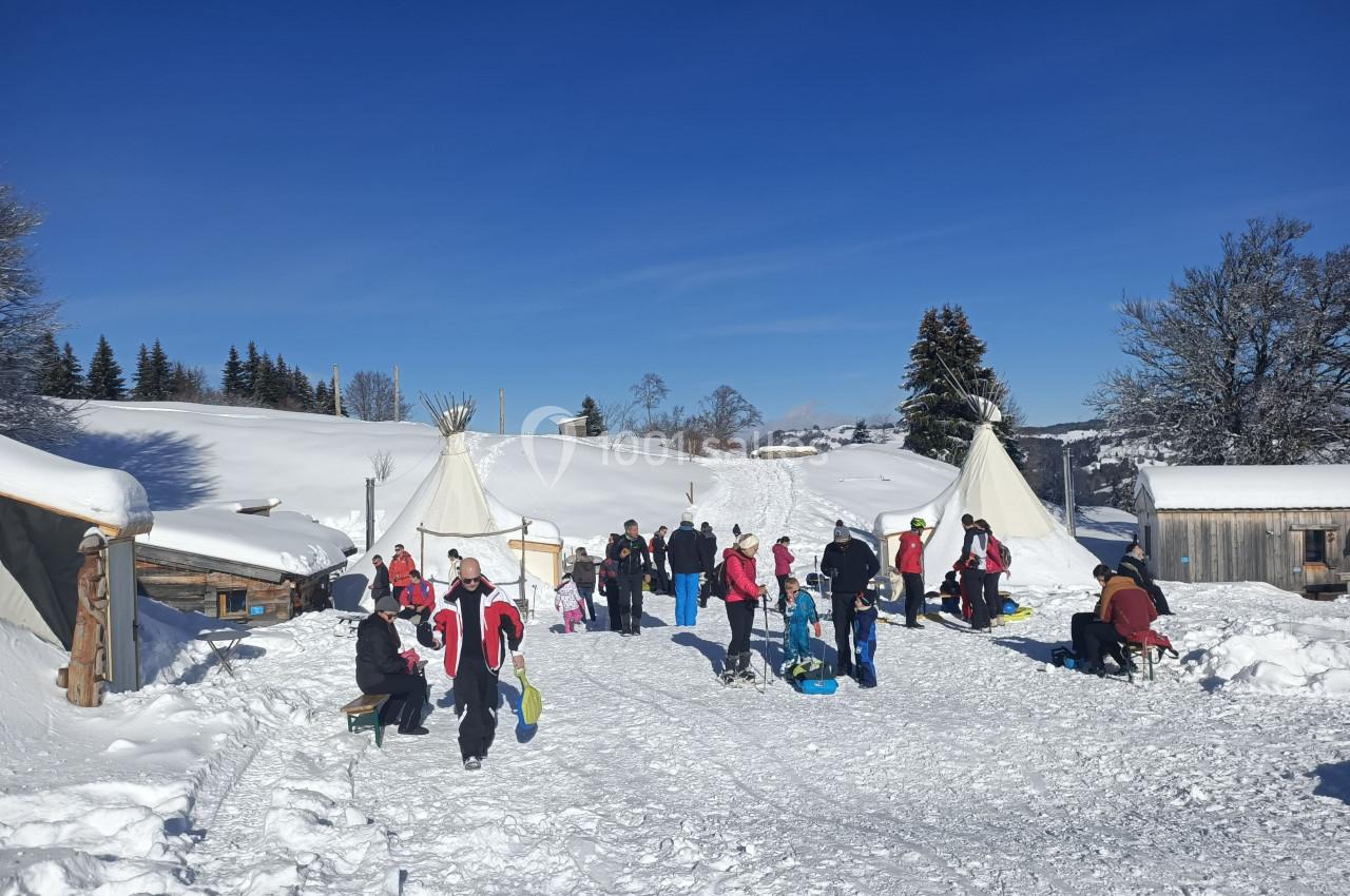 Groupe de personnes en tenue d'hiver près de tipis dans un paysage enneigé sous un ciel bleu.