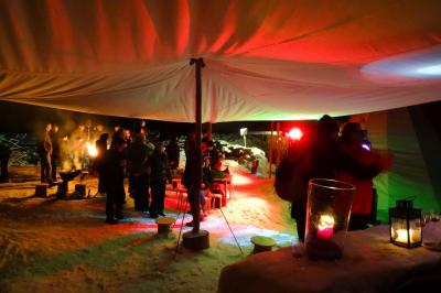 Groupe de personnes rassemblées en extérieur près de tentes et d'une table avec des verres, dans un cadre naturel.