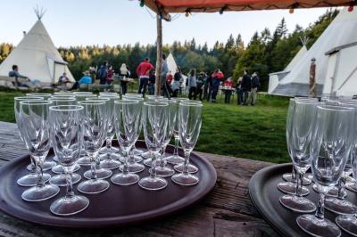Groupe de personnes rassemblées en extérieur près de tentes et d'une table avec des verres, dans un cadre naturel.