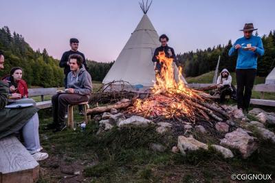 Groupe de personnes rassemblées en extérieur près de tentes et d'une table avec des verres, dans un cadre naturel.