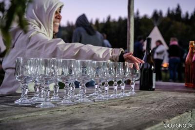 Groupe de personnes rassemblées en extérieur près de tentes et d'une table avec des verres, dans un cadre naturel.