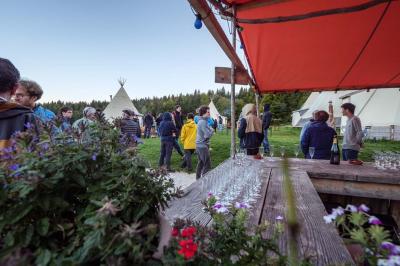 Groupe de personnes rassemblées en extérieur près de tentes et d'une table avec des verres, dans un cadre naturel.