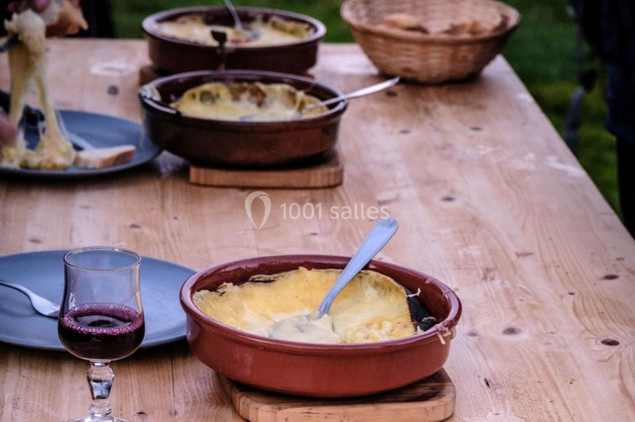 Plat de fromage fondu servi dans des ramequins en terre cuite sur une table en bois, avec du vin rouge et du pain.