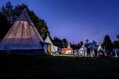 Groupe de personnes rassemblées en extérieur près de tentes et d'une table avec des verres, dans un cadre naturel.