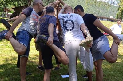 Groupe de personnes rassemblées en extérieur près de tentes et d'une table avec des verres, dans un cadre naturel.